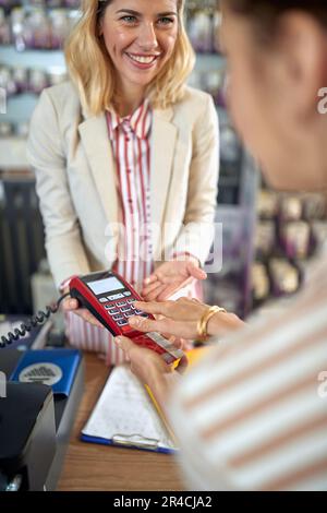 Jeune femme payant avec la carte de crédit, en entrant son code PIN, belle souriante personne de vente tenant le lecteur de carte de crédit pour le client. Shopping, style de vie c Banque D'Images