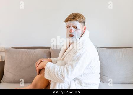 Drôle d'homme ayant le plaisir à la maison en utilisant le masque de visage pour une meilleure humeur se sentant génial. Portrait d'un gars qui fait des procédures cosmétiques. Concept de soins de la peau des personnes Banque D'Images