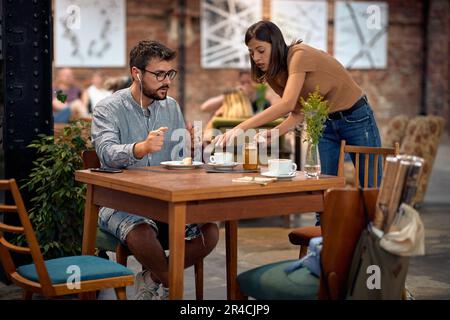 Jeunes étudiants à la cafétéria, prenant du café. Femme debout et gérant des choses sur la table, le nettoyage avec une serviette en papier. Jeunes, étudiants, café, style de vie Banque D'Images