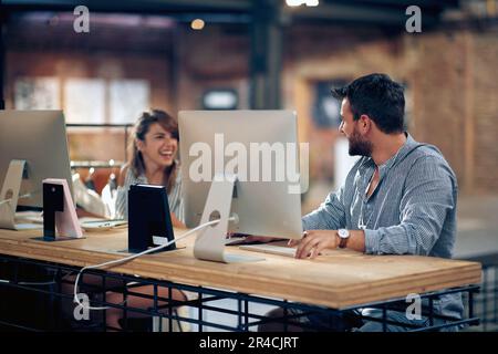 De beaux jeunes collègues s'amusent au travail, s'assoyent devant les ordinateurs et ont une conversation amusante. Entreprise, étudiants, concept de travail d'équipe. Banque D'Images