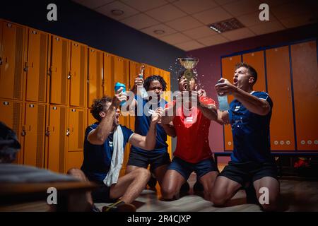 Groupe de jeunes joueurs de football célébrant ensemble le trophée d'or dans le dressing. Éclabousser l'eau et crier, se sentir joyeux. Banque D'Images