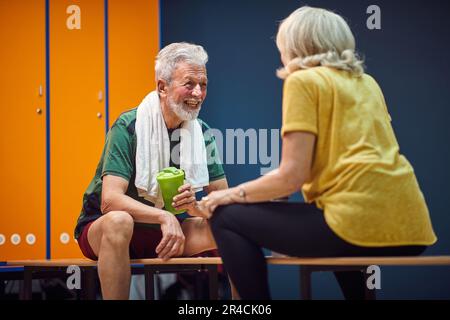 Sportif homme et femme mature dans le vestiaire de salle de gym assis face à l'autre et ayant une conversation joyeuse. Concept de vie, de santé, de style de vie pour les aînés. Banque D'Images
