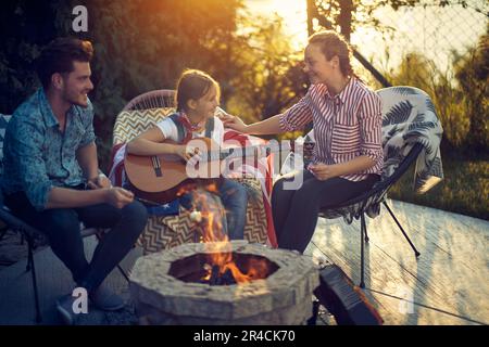 Une mère, un père et une fille se sont rassemblés autour d'un feu confortable, se livrer à la délicieuse activité de torréfaction des guimauves. Pendant ce temps, leur talent d Banque D'Images