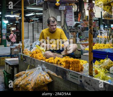 Un vendeur de fleurs fait de la guirlande de marigold à l'intérieur du marché aux fleurs de Bangkok (Pak Khlong Talat) qui sont utilisés pour la décoration de festival en Thaïlande. Marché aux fleurs de Bangkok (Pak Khlong Talad) le plus grand marché aux fleurs en gros de Thaïlande, ouvert 24 heures sur 24, 7 jours sur 7, qui jouxte un marché aux légumes frais, aux fruits et aux herbes, situé sur la route Chak Phet, près du pont commémoratif (Saphan Phut) dans la vieille ville historique. Banque D'Images