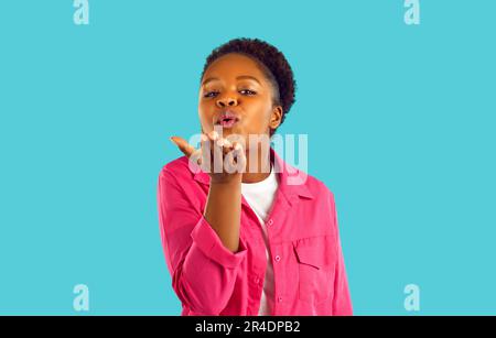 Romantique afro-américaine femme souffle un baiser à la caméra sur fond turquoise. Banque D'Images