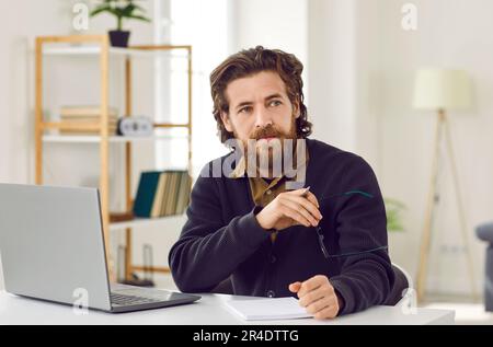 Homme d'affaires sérieux et pensif qui travaille avec un ordinateur portable et un bloc-notes en pensant à la résolution des problèmes de travail. Banque D'Images