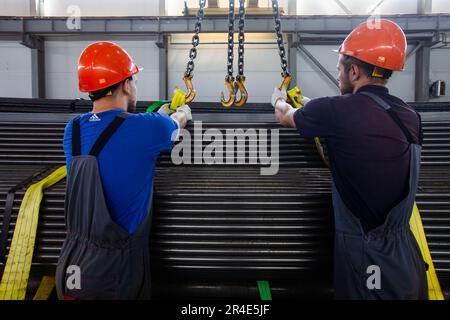 Podolsk, province de Moscou - 02 août 2021: Entrepôt de pipes. Deux ouvriers chargent les tuyaux avec un pont roulant et des sangles jaunes. Banque D'Images