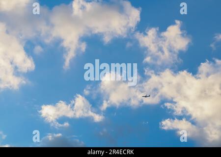 Un avion est en train de s'envoler dans le ciel bleu vif, avec des nuages blancs moelleux en arrière-plan Banque D'Images