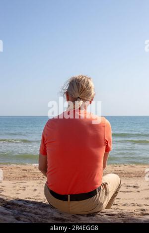 Homme dans un t-shirt et un pantalon se trouve sur une rive sablonneuse et regarde la mer. Voyages et tourisme. Banque D'Images