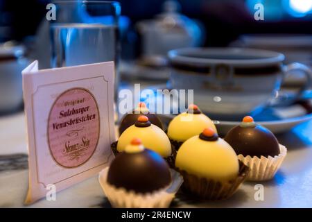 Les originaux Venusbrüstchen de Salzbourg ("Nipples de Vénus") reposent à côté d'une tasse de café sur une table à Salzbourg, en Autriche. Ludwig Rigaud a créé la praline – crème de nougat aux châtaignes marinées et une cerise Amarena, enrobée de chocolat blanc ou noir – en 1991 pour l'année Mozart, inspirée par le bonbon historique "Capezzoli di Venere" de l'époque de Mozart. Banque D'Images