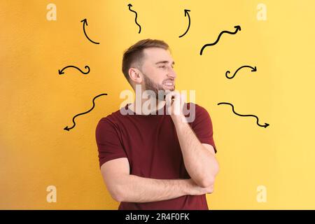 Choix dans la profession ou dans d'autres domaines de la vie, concept. Prise de décision, jeune homme entouré de flèches dessinées sur fond jaune Banque D'Images