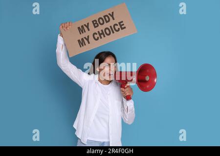 Femme émotive criant dans le mégaphone et tenant la plaque avec l'expression mon corps mon choix sur fond bleu clair. Protestation contre l'avortement Banque D'Images