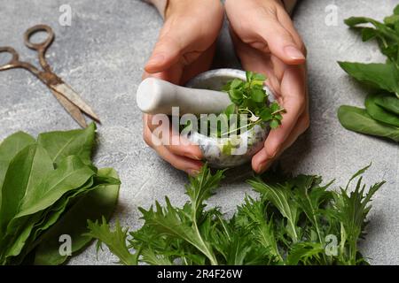 Femme moulant des herbes vertes fraîches dans le mortier à la table gris clair, gros plan Banque D'Images