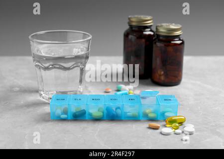 Boîte hebdomadaire avec médicaments et verre d'eau sur table en marbre gris Banque D'Images