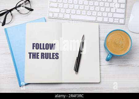 Bloc-notes avec phrase Suivez les règles, stylo, clavier d'ordinateur et tasse de café sur table en bois blanc, plat Banque D'Images