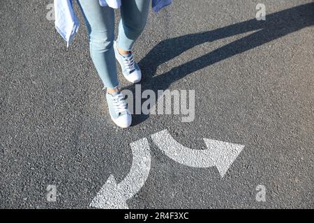 Choix. Femme marchant vers des marques tracées sur la route, gros plan. Flèches blanches pointant dans des directions opposées Banque D'Images