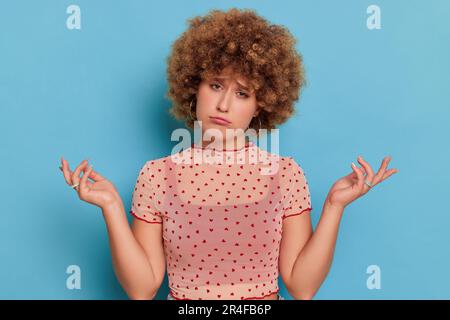 Contrarié jeune femme avec la coiffure afro posant sur fond bleu, allant pleurer et tenant les mains dans le geste sans défense, concept de moments tristes, espace de copie Banque D'Images