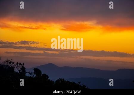 Forêt contre Panorama magnifique coucher de soleil coloré dans la campagne au-dessus des collines et des champs, beauté de la nature fond et nuages ciel Banque D'Images