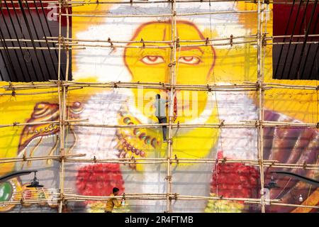 Homme debout sur un échafaudage en bambou à l'aide d'un pistolet à air comprimé pour peindre une photo de hanuman le dieu hindou sur le pont janaki setu à rishikesh Inde Banque D'Images