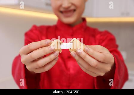 Jeune femme tenant savoureux cookie de fortune avec prédiction dans la cuisine, gros plan Banque D'Images