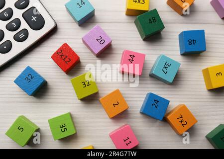 Cubes colorés avec nombres et multiplications près de la calculatrice sur table en bois blanc, plat Banque D'Images