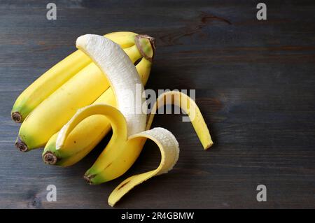 Banane pelée sur un bouquet de bananes isolées sur une table en bois brun foncé avec espace de copie Banque D'Images