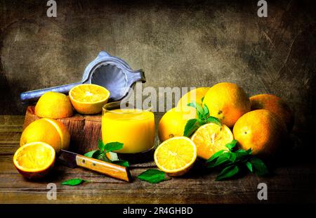 Un classique encore vivant avec de délicieuses oranges biologiques, un verre de jus d'orange frais placé ensemble sur une table rustique en bois. Banque D'Images