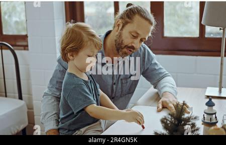 Peinture de famille caucasienne sur papier avec son à l'intérieur dans la maison. Petit fils apprendre à dessiner l'image d'art appréciez la créativité avec le père dans la maison. Banque D'Images