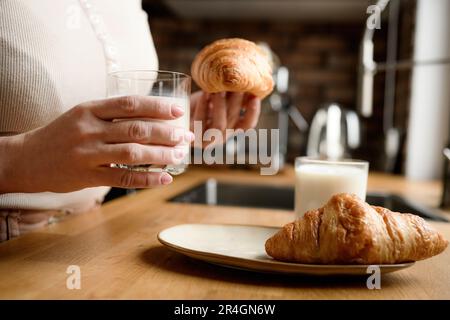 La fille a un petit-déjeuner avec du lait et des croissants dans la cuisine Banque D'Images