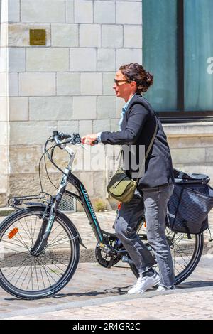 Femme poussant à vélo le long de la rue de la ville - Tours, Indre-et-Loire (37), France. Banque D'Images