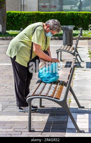 Femme en masque de visage vérifiant sac shopping sur banc de parc - Tours, Indre-et-Loire (37), France. Banque D'Images