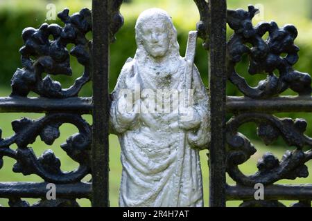 Détail d'une figure de Jésus-Christ avec un livre et un personnel entre ses mains entre une croix de métal peinte en noir, près d'une tombe dans un cimetière Banque D'Images