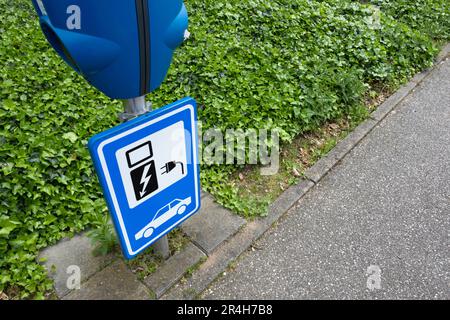Un panneau bleu avec un chargeur au-dessus de lui dans un parking le long d'une ceinture verte pour indiquer qu'il est seulement pour charger des voitures électriques. Point de charge EV Banque D'Images