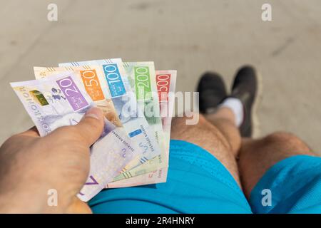 Un jeune homme assis sur un banc tient en main un paquet de couronnes suédoises, Suède, concept financier, Premier emploi, Banque D'Images