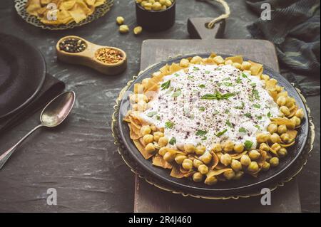 Cuisine arabe ; authentique libanais « Fattah » ou « Fatteh » avec pain pita grillé, pois chiches et sauce au yaourt sur fond sombre rustique. Banque D'Images