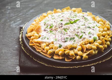 Cuisine arabe ; authentique libanais « Fattah » ou « Fatteh » avec pain pita grillé, pois chiches et sauce au yaourt sur fond sombre rustique. Banque D'Images