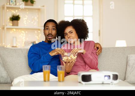 Des conjoints africains choqués regardant un film enrageant du popcorn à l'intérieur Banque D'Images