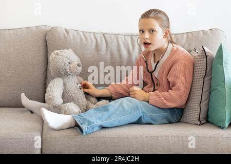 Choqué drôle caucasien petite fille jouant docteur avec l'ours jouet, écoute à respirer avec le stéthoscope Banque D'Images