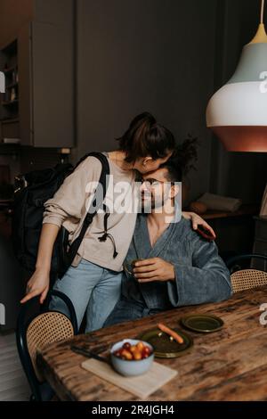 Personne non binaire embrassant petit ami assis à la table à manger dans la chambre Banque D'Images