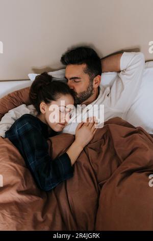 Vue en grand angle de l'homme embrassant personne non binaire se relaxant dans le lit à la maison Banque D'Images