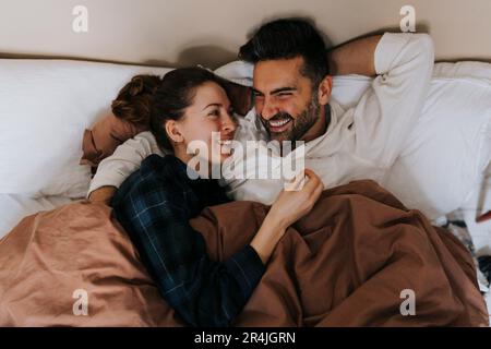 Personne joyeuse non binaire parlant avec un ami en étant allongé sur le lit à la maison Banque D'Images