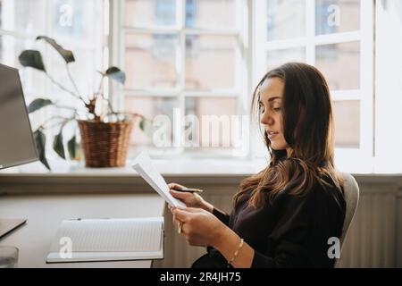 Vue latérale d'une femme d'affaires examinant un document assis au bureau Banque D'Images