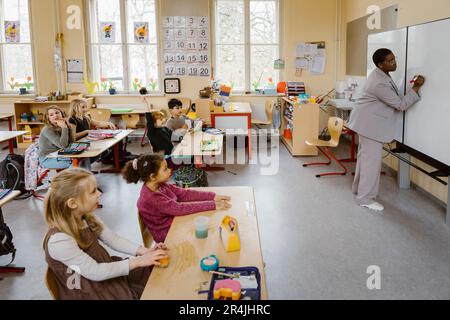 Les élèves qui regardent la rédaction des enseignants sur un tableau blanc en classe Banque D'Images