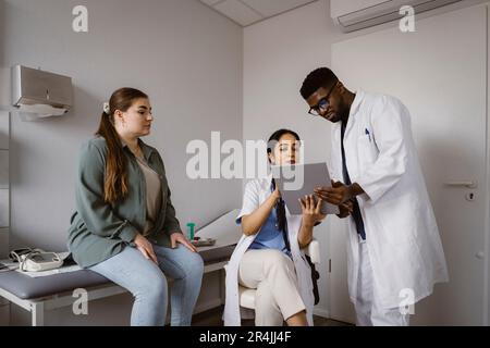 Les professionnels de la santé, hommes et femmes, discutent au sujet d'un PC tablette avec une patiente en clinique Banque D'Images