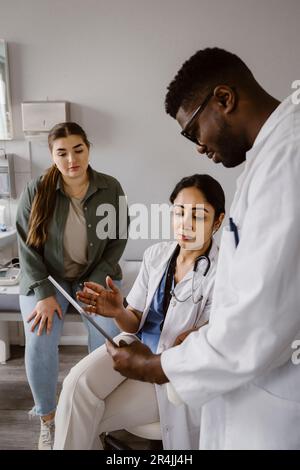 Médecin expliquant à un collègue un PC tablette en clinique Banque D'Images