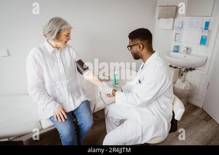 Jeune médecin de sexe masculin vérifiant la pression artérielle de la patiente à la clinique Banque D'Images