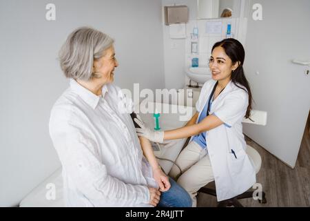 Une femme souriante qui consulte un patient senior dans la salle d'examen de la clinique Banque D'Images