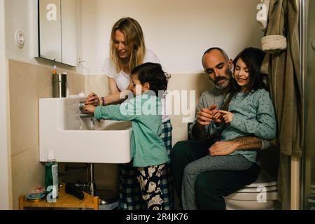 Femme aidant le fils avec se laver les mains tandis que l'homme et la fille parlant dans la salle de bains Banque D'Images