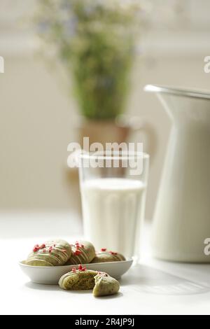 Composition avec biscuits maison au pain d'épice à la menthe avec matcha et fraises sublimées dans une assiette, verre de lait, pot et fleurs sauvages dans un vase sur la ba Banque D'Images