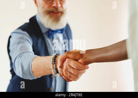 Homme excentrique et élégant avec une barbe et une moustache qui se secouent les mains d'une femme africaine. La poignée de main est la mise au point, le visage de l'homme est flou, et le b Banque D'Images